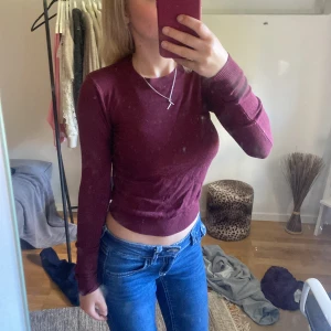 Vinröd croppad långärmad topp - Säljer en vinröd croppad topp med lång ärm. Toppen har en slim passform och är tillverkad i ett mjukt, stickat material som sitter snyggt mot kroppen. Perfekt att styla med jeans eller kjol för en cool och enkel look.