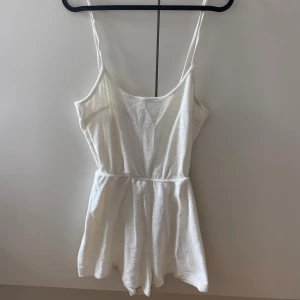 Vit kort byxdress från Divided XS - Supersöt vit kort klänning från Divided i storlek XS. Klänningen har tunna axelband och markerad midja, perfekt för varma dagar. Tillverkad i mjuk frotté som känns skön mot huden och ger en avslappnad vibe.