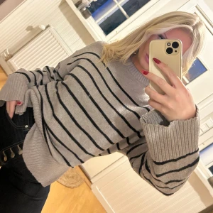 Grå randig stickad tröja - Säljer en grå stickad tröja med svarta horisontella ränder. Tröjan har ribbad mudd vid hals, ärmslut och nederkant, samt långärmad och loose passform. Perfekt för dig som gillar enkel och stilren look med lite oversized vibe. Storlek M men passar även en S💖💖🌸🌸