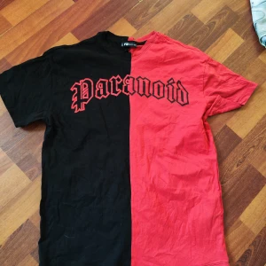 Svart och röd t-shirt från FB Sister - Cool t-shirt från FB Sister i storlek XS med delad design – ena halvan är svart och andra röd. Trycket 'Paranoid' i gotisk stil över bröstet ger en edgy vibe. Tillverkad i mjuk bomull och har klassisk rund hals och korta ärmar.