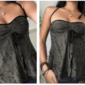 Svart glittrig linnetopp med snörning - Säljer en svart glittrig linnetopp med tunna axelband och snygg snörning framtill. Toppen har en lätt rynkad byst och ett glittrande tyg med slitna detaljer som ger en cool look. Perfekt för dig som gillar trendiga och unika plagg.
