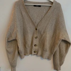 Beige ribbad kofta från Bik Bok - Supermysig beige ribbad kofta från Bik Bok i storlek XL men känns som M. Koftan har v-ringning, stora knappar framtill och är croppad med lång ärm. Perfekt att slänga på sig när det är lite kyligt ute.