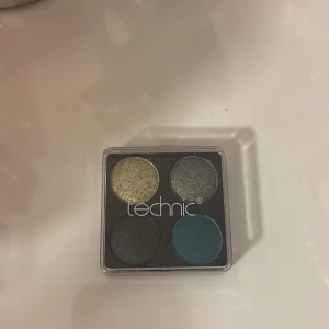 Technic ögonskuggspalett 4 färger - Palett med fyra ögonskuggor från Technic. Innehåller en glittrig guld, skimrande silvergrå, matt svart och en djup turkosblå nyans. Perfekt för att skapa både dramatiska och kreativa ögonlooker. Kompakt och smidig för necessären.