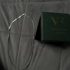 Silverfärgat halsband & armband Viktor Frisk - Säljer ett stilrent set med halsband och armband från Viktor Frisk x Guldfynd. Båda smyckena är i silverfärg med klassisk kedjedesign och levereras i original grön ask. Perfekt för dig som gillar minimalistiska accessoarer med modern känsla. Äkta silver. Skriv pris förslag vid intresse.