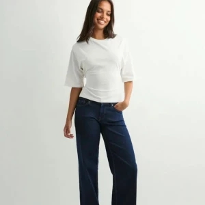 Vit croppad topp med knyt i ryggen - Säljer en vit croppad topp med korta ärmar och snygg öppen rygg som knyts med en stor rosett. Toppen har en enkel och clean look framtill och är tillverkad i mjuk bomull. Perfekt för dig som gillar trendiga detaljer och vill sticka ut lite extra.