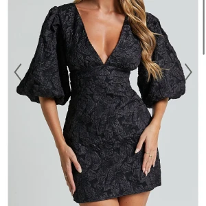 Svart kort klänning med puffärmar - Supersnygg svart kort klänning med djup v-ringning och stora puffärmar. Klänningen har ett strukturerat blommönster i tyget och markerad midja som ger en riktigt trendig siluett. Aldrig använd