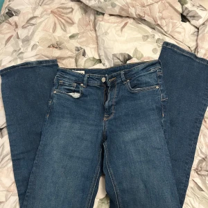 Blå bootcut jeans från Zara, stl 38 - Säljer ett par klassiska blå bootcut jeans från Zara i storlek 38. Jeansen har fem fickor, normal midja och snyggt utsvängda ben. Tillverkade i mjukt denimtyg med gul kontrastsöm och läderpatch bak i midjan.