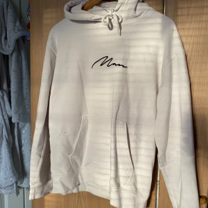 Beige hoodie från boohooMAN - Säljer en stilren beige hoodie från boohooMAN i storlek S. Tröjan har huva med snörning, känguruficka och svart broderad logga på bröstet. Perfekt för en chill och avslappnad look.