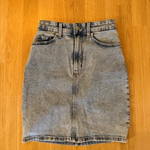 Jeanskjol  - Kort jeanskjol i ljus tvätt med klassisk femficksmodell. Skjolen har en rak passform och en bekväm midjehöjd. Perfekt för en avslappnad men stilren look. Storlek 32