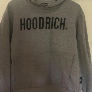 Grå hoodie Hoodrich  - Säljer en grå hoodie från Hoodrich i 100% bomull. Tröjan har svart text