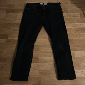 Svarta Tommy Hilfiger Denton Stretch jeans - Svarta jeans från Tommy Hilfiger, modell Denton Stretch Straight Fit. Klassisk femficksdesign med raka ben och diskret Hilfiger-detalj på fickan. Jeansen har stretch för extra komfort och snygg passform. Perfekta för dig som gillar stilrena och tidlösa byxor.