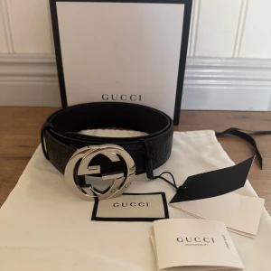 Gucci Bälte - Säljer nu mitt fina bälte från Gucci med präglad logga längs hela remmen och ett stort, rundat GG-spänne i blankt silver. Bältet är gjort i äkta skinn och har en exklusiv känsla som lyfter vilken outfit som helst. Kommer med originalpåse och etiketter. Använd fåtal gånger!