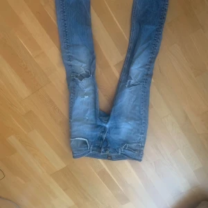 Blå slitna jeans från Lee W32 L32 - Säljer ett par blå jeans från Lee, modell Luke, med slitningar och hål på knäna för en riktigt avslappnad vibe. Jeansen har klassisk femficksdesign och är tillverkade i bomull med lite elastan för extra stretch. Perfekta för dig som gillar en streetig look.