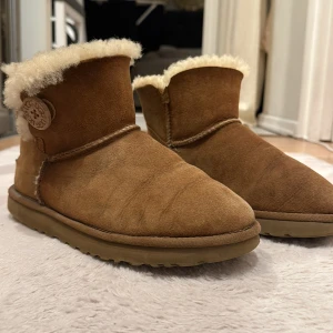 Bruna UGG boots med fårull - Mysiga bruna UGG boots i mocka med fluffig fårullskant och insida. Skorna är i bra använt skick förutom defekt kolla 3 bilden. Dom är i storlek 38,skriv vid funderingar 