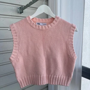 Ljusrosa stickad väst från Zara - Superfin ljusrosa stickad väst från Zara med bred ribbad kant vid hals, ärm och nederkant. Västen är croppad och har en klassisk, enkel design som är lätt att styla över en skjorta eller t-shirt. Perfekt för lager-på-lager-look!
