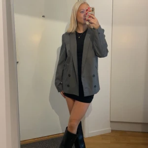 Grå oversized kavaj med knappar - Snygg grå kavaj i oversized modell med dubbelknäppning. Kavajen har svarta knappar och raka fickor framtill. Perfekt att styla med boots och klänning 