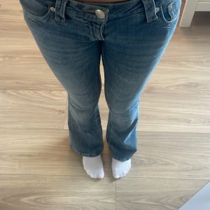True Religion bootcut jeans blå, stl 26 - Säljer ett par klassiska blå jeans från True Religion i bootcut-modell. Jeansen har snygga kontrastsömmar, ikonisk bakficka och rosa sömmar💕 Använda 2 gånger