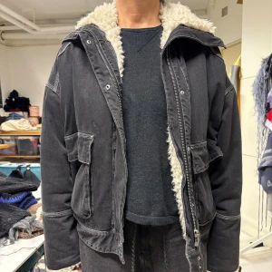 Mörkgrå jacka med teddyfoder - Mörkgrå jacka i jeans med teddy foder, bomberjacka passform. Jackan har stora fickor framtill, dragkedja och tryckknappar . Kragen kan knäppas hela vägen upp eller vikas ner. Från & other stories.