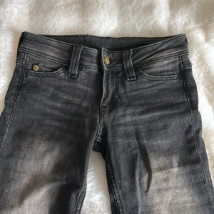 Svarta bootcut jeans från Cheap Monday - Snygga svarta jeans från Cheap Monday med bootcut-ben och klassisk femficksdesign. Jeansen har en cool tvättad look och en stor orange logga bak i midjan. Jeansen är aldrig använda, säljer pga att dom är försmå.