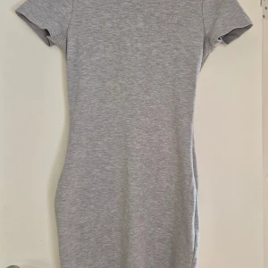 Grå kortklänning Tiger of Sweden - Snygg grå kortklänning från Tiger of Sweden, modell Lorah. Klänningen har korta ärmar, figurnära passform och en cool öppen ryggdetalj. Tillverkad i en mjuk mix av viskos, polyamid och elastan. Tight modell.