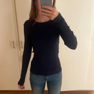 Mörkblå långärmad tröja i bomull - Enkel och stilren mörkblå långärmad tröja i mjuk bomull. Tröjan har en tight passform och rund halsringning, perfekt att matcha med jeans eller kjol för en clean look.