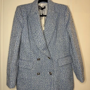 Blåvit kavaj från Zara i storlek L - Snygg blåvit kavaj från Zara i storlek L. Blazern har dubbelknäppning med silvriga knappar, klassisk krage och två fickor framtill. Materialet är grovt vävt och ger en exklusiv känsla. Perfekt för dig som vill sticka ut med en trendig och stilren look.