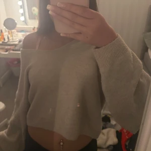 Beige croppad stickad tröja - Supermjuk beige stickad tröja med croppad passform och offshoulder-design. Tröjan har långa ärmar och bred ribbad mudd vid ärmslut.