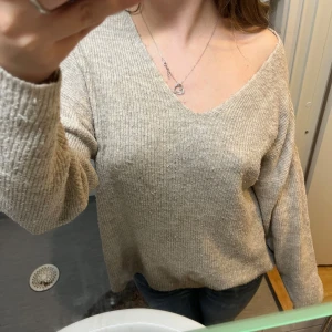 Beige ribbad stickad tröja Vero Moda - Mysig beige stickad tröja från Vero Moda med ribbad struktur och v-ringad hals. Tröjan har en loose passform och långa ärmar, perfekt för lager på lager under kyliga dagar. Enkel att matcha med jeans eller kjol för en chill look.