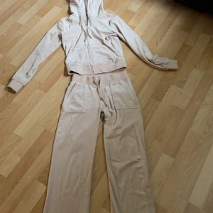 Beiga mjukisbyxor med snörning - Säljer ett par beiga mjukisbyxor från Juicy Couture i mjuk velour med bred resår och snörning i midjan. Byxorna har raka ben, stora fickor framtill och broderad JC-logga på ena fickan. Perfekta för chill dagar eller när du vill vara extra bekväm.