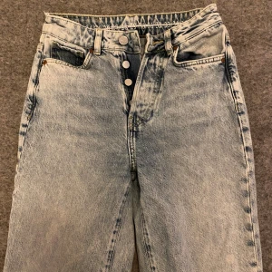 Ljusblåa wide jeans med slitna knän - Ljusblåa jeans från Bilbok med hög midja och raka, vida ben. Jeansen har slitna detaljer och hål vid vid knäna. Jeansen har använts mycket men inte påverkats i kvaliten, har också en liten fläck nere vid ena benet på baksidan. Är 163 och byxorna passar, skulle säga att byxorna passar en xs/s 