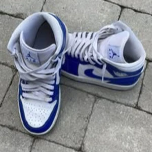 Nike Air Jordan 1 mid blå/vit EUR 39 - Säljer ett par Nike Air Jordan 1 mid i blått och vitt. Klassisk siluett med snörning, rund tå och ikoniska vingar-loggan på sidan. Ovandel i skinn och syntet, vit bas med blå detaljer och swoosh. Perfekta för dig som vill sticka ut med en tidlös sneaker.