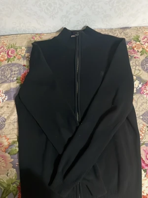 Svart ziptröja med hög krage - Säljer en svart ziptröja med hög krage och långa ärmar. Tröjan har en hel dragkedja framtill och är tillverkad i ett mjukt, stickat material. Perfekt för lager på lager. Fråga gärna om vill se något specifikt med koftan