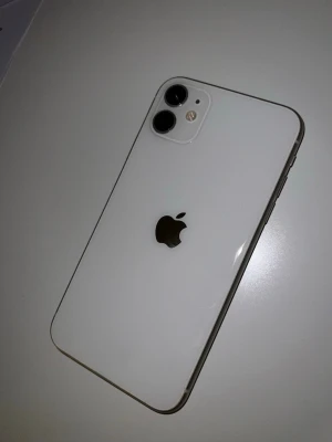 Vit iPhone 11 med dubbla kameror - Snygg vit iPhone 11 med stilren glasbaksida och två kameror i hörnet. Klassisk Apple-logga i mitten och rundade kanter. Perfekt för dig som gillar modern design och vill ha en pålitlig smartphone. 74% batterihälsa och varsamt använd! Pris går att diskutera.