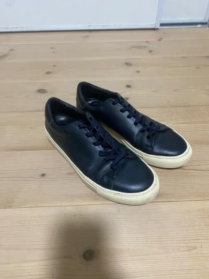 Svarta sneakers från Sandro - Stilrena svarta sneakers från Sandro med ovandel i skinn och klassisk vit sula. Skorna har rund tå, svarta snören och minimalistisk design som passar till det mesta. Perfekta för dig som gillar en clean och modern look.