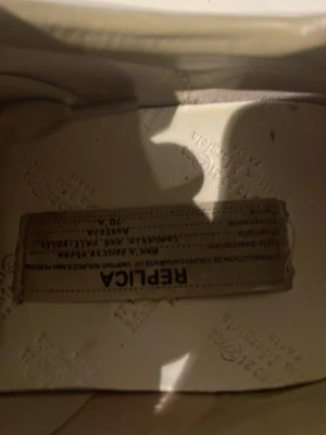 Maison Margiela sneakers med färgstänk - Unika sneakers från Maison Margiela med beige och vita paneler, klassisk gummisula och färgstänk i rött, blått, gult och grönt. Skorna har snörning och en rund tå. Perfekta för dig som vill sticka ut med din stil. Finns box med. Pris ej hugget i sten