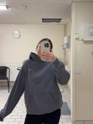 Hoodie - Säljer en grå/gråblå hoodie från ICW med klassisk känguruficka och liten vit logga på bröstet. Hoodien har huva och ribbade muddar vid ärmslut och nederkant. Perfekt för både vardag och träningspass.