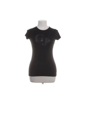 Svart vintage Guess t-shirt med stenar - Snygg vintage svart t-shirt från Guess med korta ärmar och tight passform. Framtill finns ett stort 'GJ'-tryck i glittrande strass som ger en extra touch. Tillverkad i mjuk bomull som känns skön mot huden. Perfekt för dig som gillar stilrena plagg med lite bling. Saknar några stenar. Priset går att diskutera🦢🌸🫶🏼