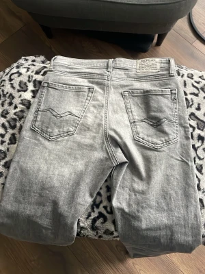 Replay ljusgrå jeans straight fit - Säljer ett par ljusgrå jeans från Replay med klassisk femficksmodell och raka ben. Jeansen har snygga slitningar och Replay-logga på bakfickan. Perfekta för dig som gillar en clean och avslappnad stil.