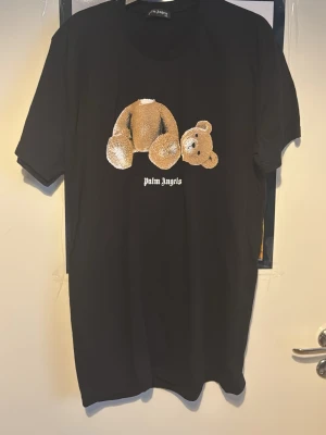 Svart Palm Angels t-shirt med björn - Svart t-shirt från Palm Angels med ikoniskt nalletryck på framsidan och stor Palm Angels-logga i vitt på ryggen. Klassisk passform och rund hals. Tillverkad i mjuk bomull, perfekt för en trendig streetwear-look. Storleken är XXL men passar XL