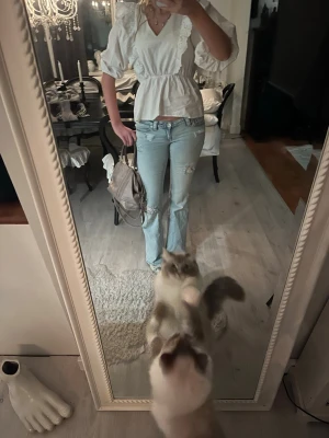 Vit blus med volang och v-ringning - Säljer en söt vit blus med v-ringning och volangdetaljer framtill. Blusen har puffiga korta ärmar och markerad midja som ger en feminin siluett. Perfekt för dig som gillar romantisk och trendig stil.