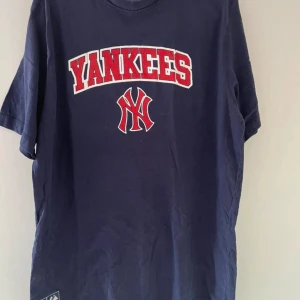 Mörkblå Yankees t-shirt, herr storlek XL - Snygg mörkblå t-shirt från Yankees med röd och vit logga framtill och tryck i nacken. Klassisk rund hals och korta ärmar. Perfekt för dig som gillar sportig streetstyle och vill sticka ut med en ikonisk look.
