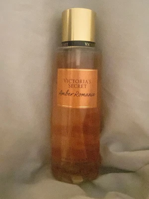 Victoria's Secret Amber Romance parfym - Amber Romance från Victoria's Secret är en parfym i en elegant, genomskinlig plastflaska med guldigt lock. Flaskan har en varm bärnstensfärgad ton och etiketten är i matchande guld och orange. Doften är känd för sina söta och sensuella noter.