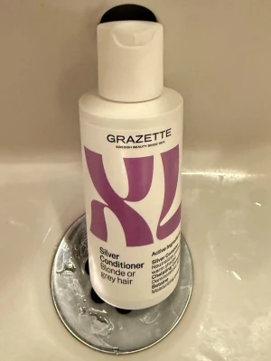 Grazette Silver Conditioner XL - Silverbalsam från Grazette i XL-flaska, speciellt för blont eller grått hår. Flaskan är vit med lila tryck och har en praktisk tryckkork. Innehåller silversubstanser som neutraliserar gula toner och ger extra fukt till håret.