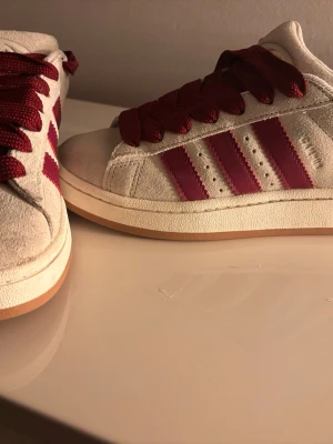 Adidas Campus sneakers beige och vinröd - Snygga Adidas Campus sneakers i beige mocka med vinröda detaljer och klassiska tre ränder på sidan. passar jätte bra som storlek 37, väldigt sparsamt användt