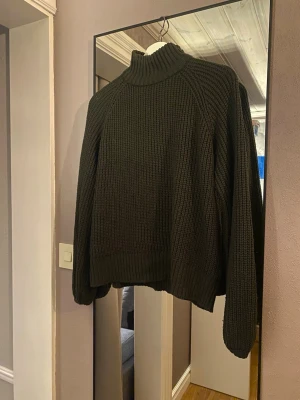 Mörkgrön stickad polotröja - Säljer en mörkgrön stickad polotröja med bred ribbad struktur. Tröjan har hög krage, långa ärmar och avslappnad passform. Perfekt för kalla dagar och enkel att styla till jeans eller kjol.