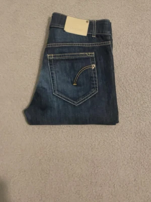 Mörkblå dondup jeans - Säljer ett par mörkblå dondup jeans med klassisk femficksdesign. Jeansen har en rak passform och är tillverkade i slitstarkt denimtyg. Perfekta för dig som gillar en tidlös och clean stil.