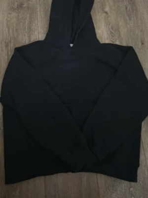 Svart basic hoodie med magficka - En enkel svart hoodie med klassisk huva och stor magficka framtill. Hoodien har en avslappnad passform och är tillverkad i mjukt material, perfekt för chill dagar. 