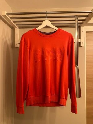 Röd sweatshirt från Hugo Boss - Snygg röd sweatshirt från Hugo Boss med broderad logga på bröstet. Tröjan har rund halsringning, långa ärmar och ribbade muddar vid ärmslut och nederkant. Perfekt för en avslappnad och trendig stil.