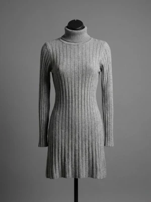 58% Viscose  poloklänning från Mezzo - Säljer en snygg grå ribbad klänning från Mezzo, tillverkad i Italien. Klänningen har polokrage, lång ärm och är stickad i mjukt material med viskos, PBT och angora. Den är kort i modellen och har en slim passform som framhäver siluetten.