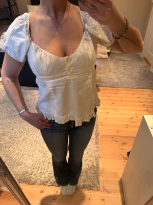 Vit blus med puffärm och volang från Brandy Melville  - Söt vit blus med puffärmar och volangkant nedtill. Djup v-ringning och lätt rynkade detaljer vid bysten ger en feminin look. Tillverkad i ett tunt, mjukt bomullstyg som känns luftigt och skönt. Perfekt att styla med jeans eller kjol.